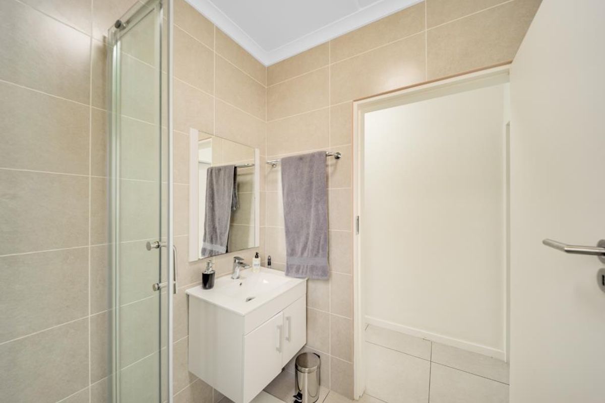 A modern, well-maintained bathroom featuring a glass shower enclosure, a white vanity cabinet with a basin, and neutral wall and floor tiling.