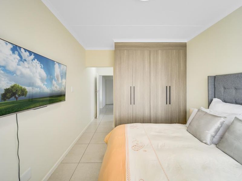 A well-maintained bedroom featuring neutral tiled flooring and modern built-in cupboards with sleek vertical handles.