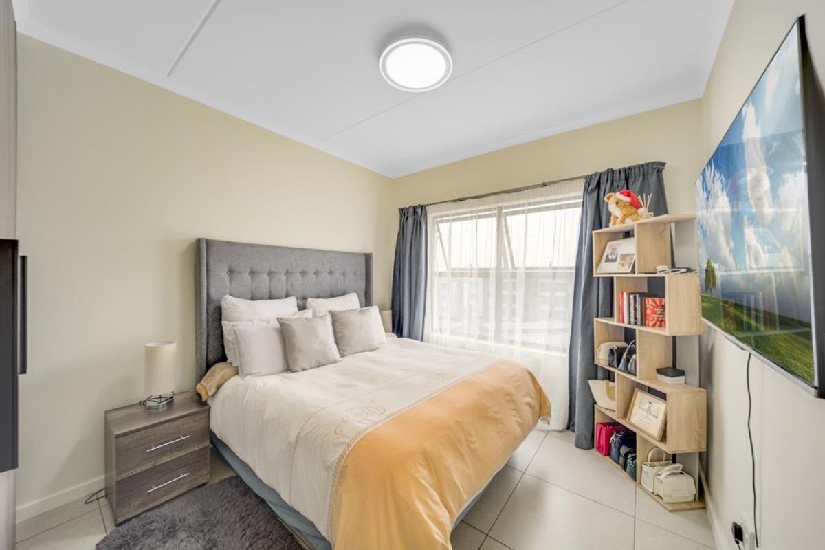 A well-maintained bedroom featuring neutral wall tones, tiled flooring, and a large window that allows for ample natural light.