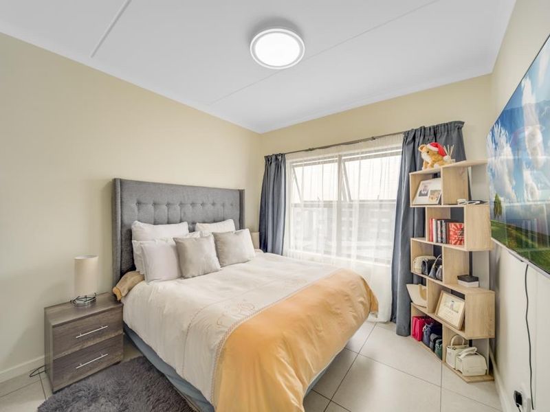 A well-maintained bedroom featuring neutral wall tones, tiled flooring, and a large window that allows for ample natural light.
