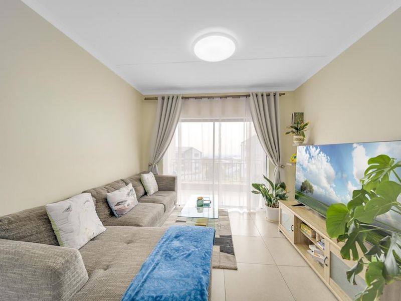 A bright and well-maintained living room featuring neutral tiled flooring and a large sliding glass door that provides access to the balcony.