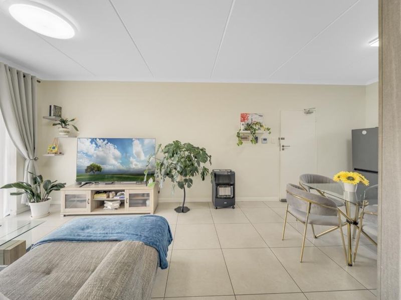An open-plan living and dining area featuring neutral tiled flooring, a sliding glass door for natural light, and a clean, well-maintained interior finish.