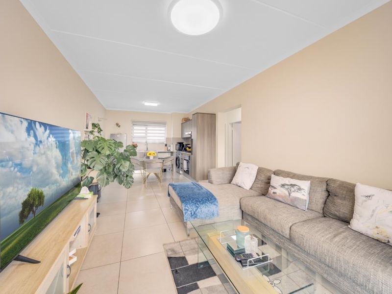 Spacious open-plan living area featuring tiled flooring, a modern kitchen with built-in cabinetry, and integrated appliances, creating a functional and cohesive living space.