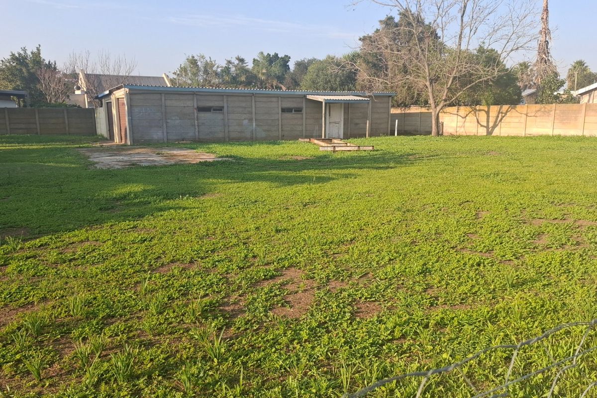 Spacious rear garden area featuring a large lawn, perimeter precast concrete walling, and a detached outbuilding structure.