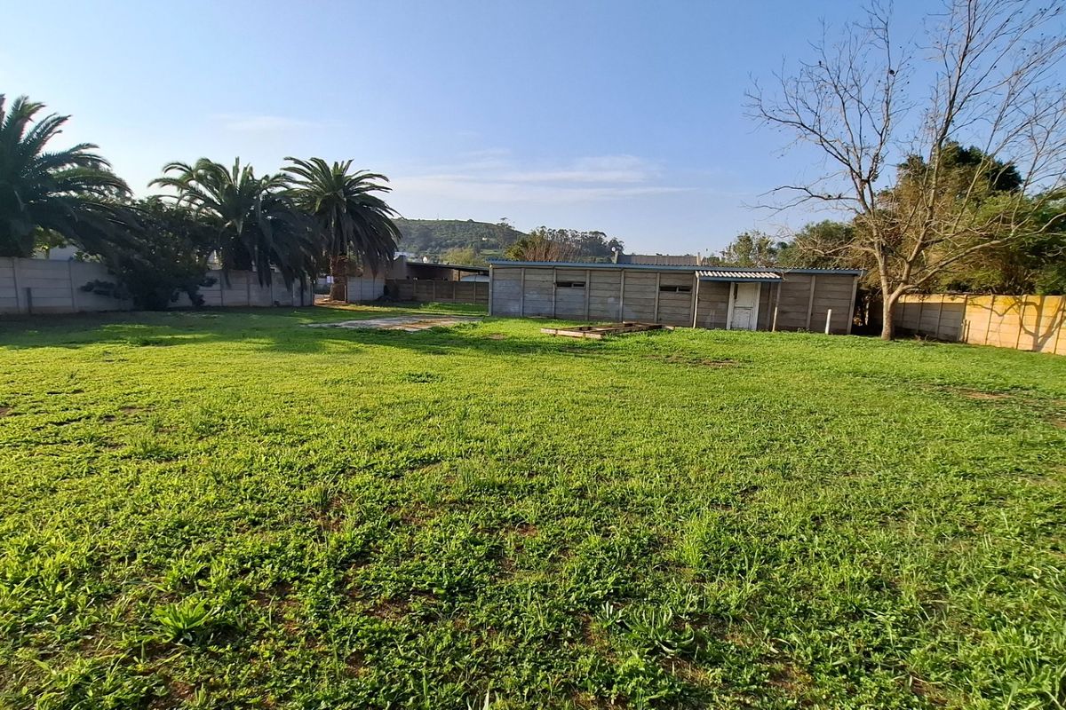 A spacious backyard featuring a large lawn area, perimeter precast concrete walling, and a detached outbuilding structure.