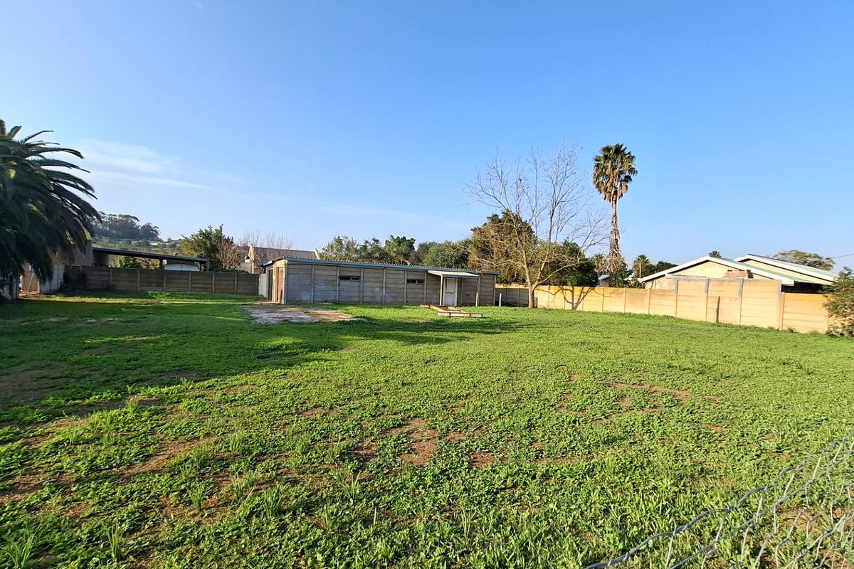 A spacious backyard area featuring a large lawn, perimeter precast concrete walling, and a detached outbuilding structure.