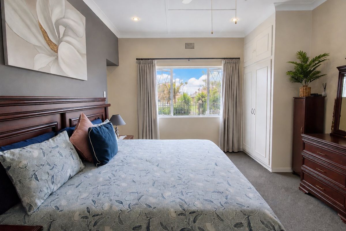 A well-maintained bedroom featuring neutral walls, carpeted flooring, a built-in wardrobe, and a ceiling fan, offering a comfortable and functional living space.