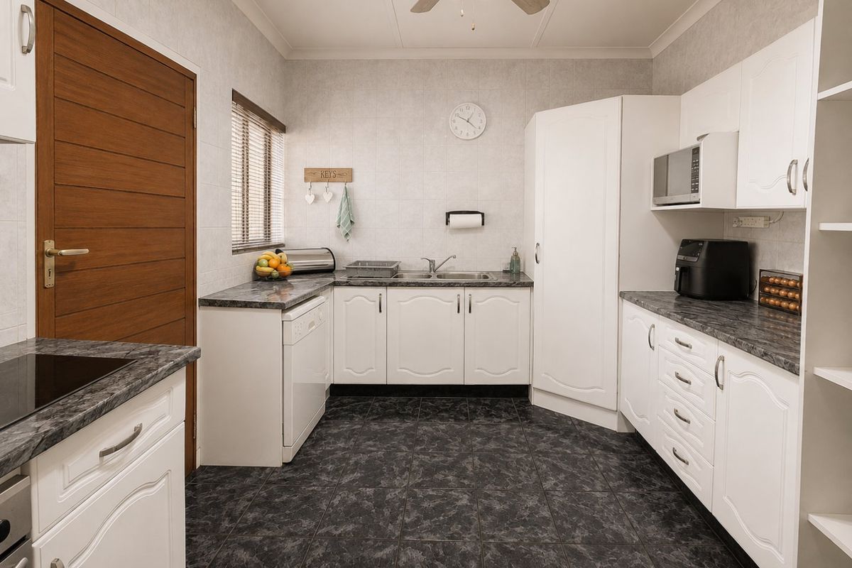 A functional kitchen featuring white cabinetry, dark laminate countertops, tiled flooring, and a built-in microwave, offering a clean and practical workspace.