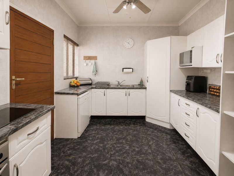 A functional kitchen featuring white cabinetry, dark laminate countertops, tiled flooring, and a built-in microwave, offering a clean and practical workspace.
