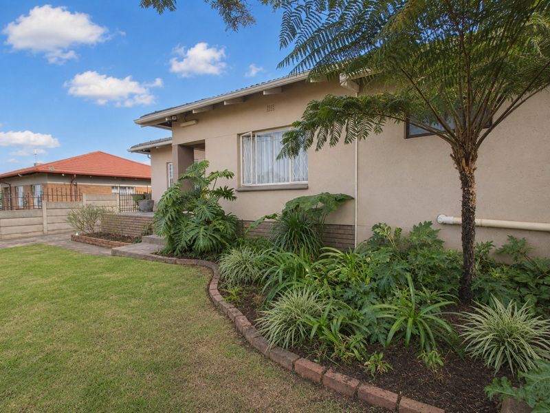 A well-maintained front exterior view of the house featuring a landscaped garden with brick edging, a paved driveway, and a secure boundary wall.