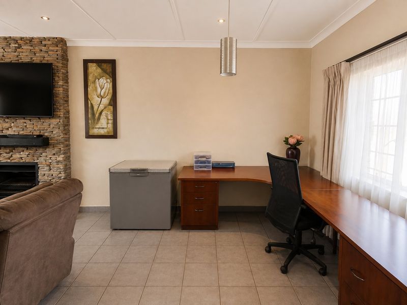 Living area featuring a stone-clad fireplace, tiled flooring, and a built-in wooden desk workspace with integrated cabinetry.