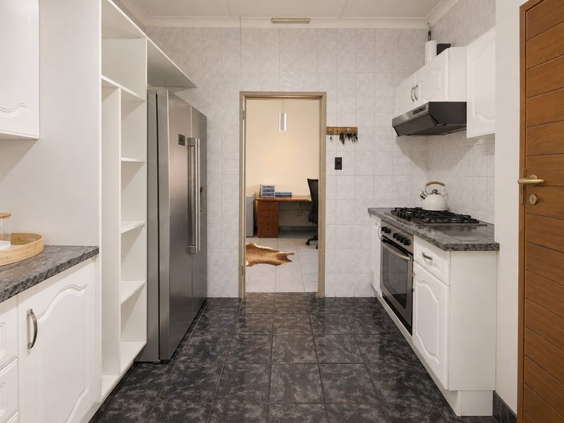A functional scullery featuring built-in cabinetry, a gas hob, oven, extractor fan, and durable tiled flooring, providing efficient additional prep and storage space.
