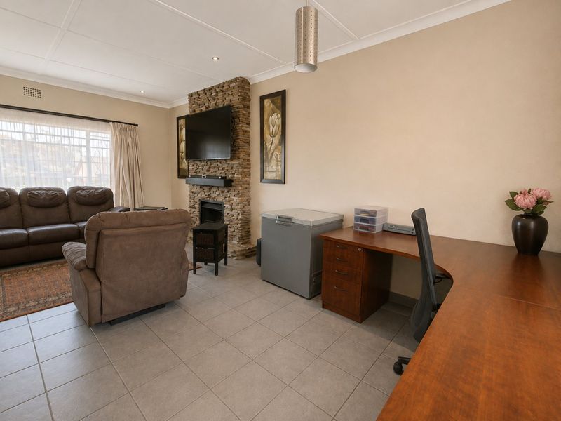 Spacious living area featuring a prominent stone-clad fireplace, neutral tiled flooring, and recessed lighting, offering a versatile layout for relaxation and home office use.