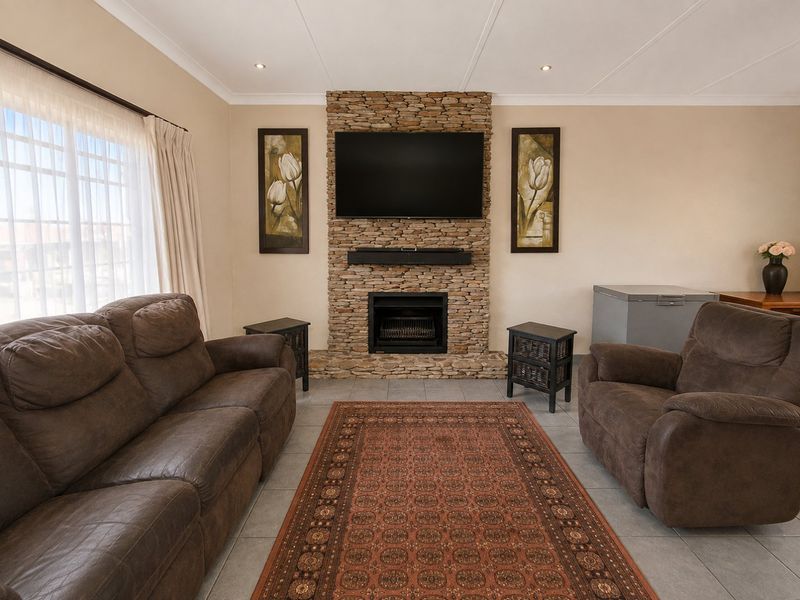 A comfortable living room featuring a prominent stone-clad fireplace, tiled flooring, and recessed lighting, creating a warm and inviting atmosphere.