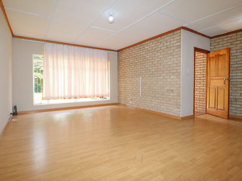 Spacious living room featuring laminate flooring, an exposed brick feature wall, and a classic timber door, offering a blank canvas for interior design.