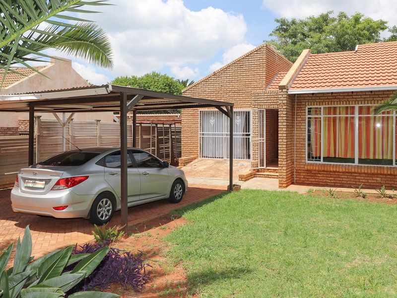Front view of a face brick house featuring a paved driveway, a covered carport, and a well-maintained front garden.
