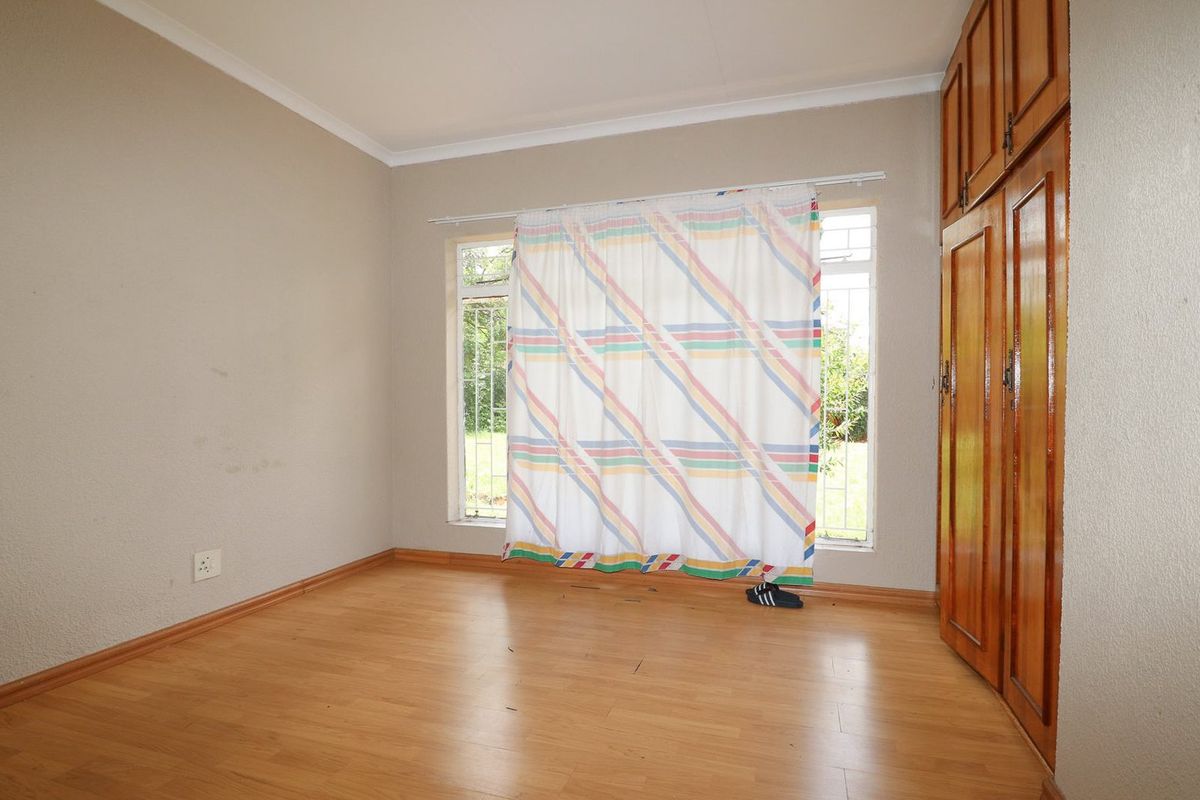 A vacant bedroom featuring laminate flooring, built-in wooden cupboards, and security bars on the windows.