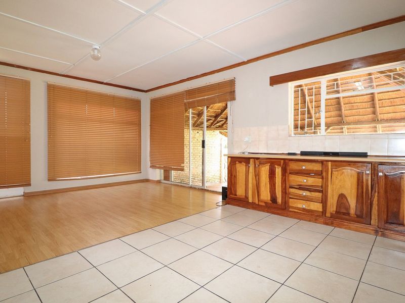 Open plan living area featuring a combination of tiled and laminate flooring, wooden cabinetry, and direct access to an outdoor patio area.