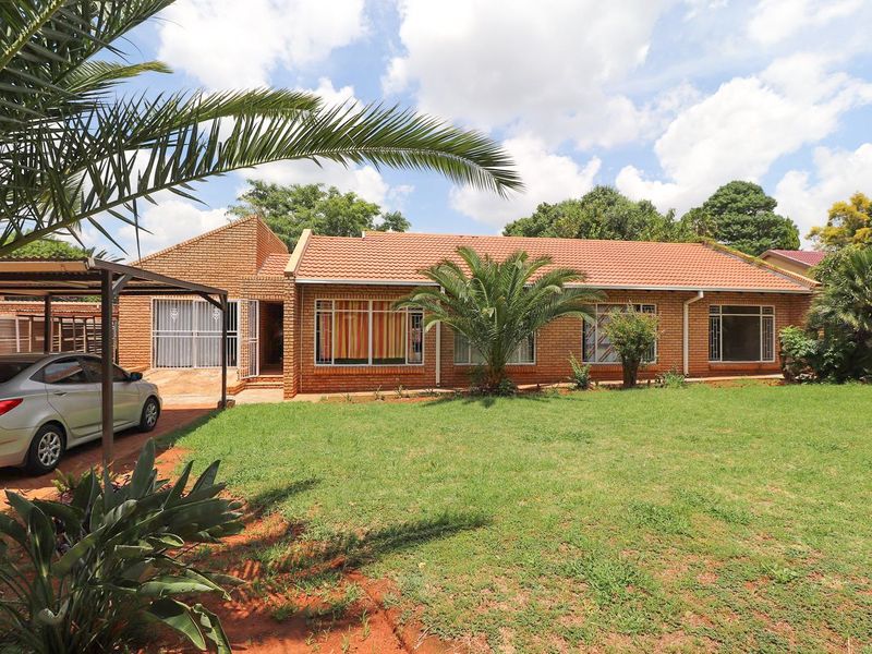 Front view of a single-story face brick house featuring a tiled roof, large windows, and an attached carport set within a spacious garden.