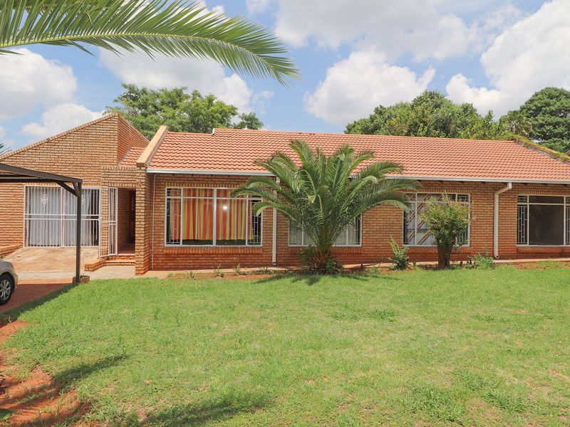A well-maintained single-story face brick house featuring a tiled roof, a front carport, and a spacious front lawn.
