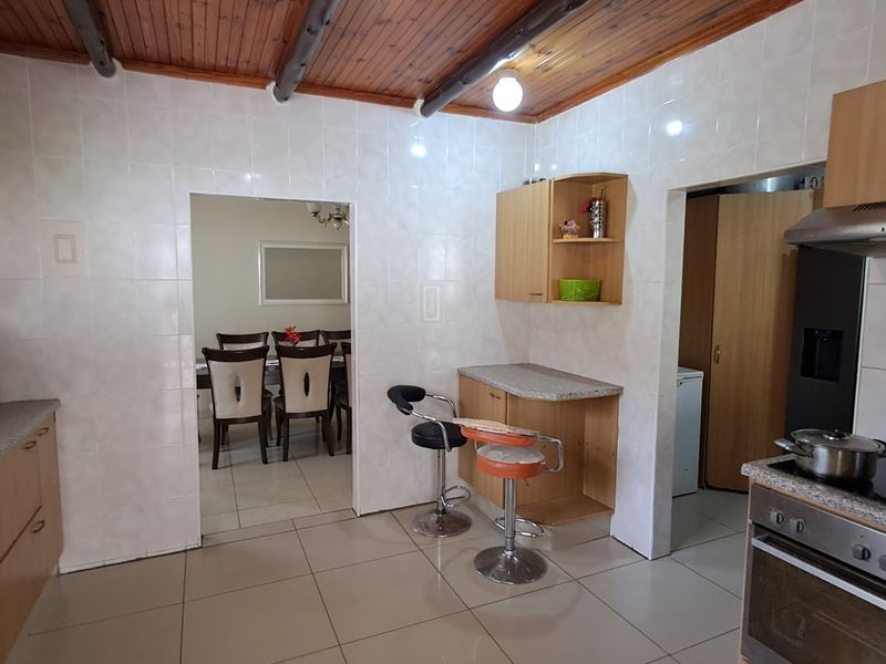 A functional kitchen featuring built-in cabinetry, tiled walls, and a timber ceiling, with an adjacent dining area visible through the doorway.