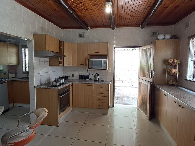 Functional kitchen featuring built-in cabinetry, granite countertops, integrated appliances, tiled flooring, and a distinctive timber ceiling with exposed beams.