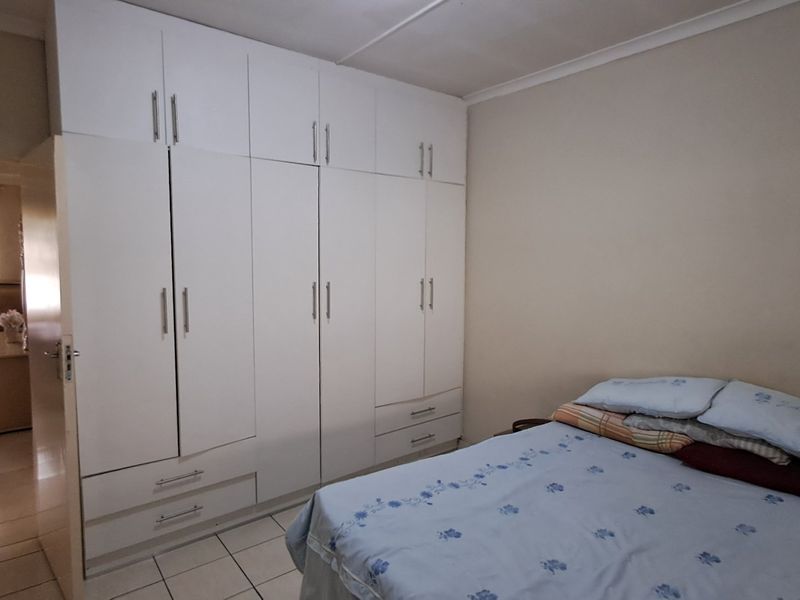 A bedroom featuring extensive white built-in cupboards with integrated drawers and tiled flooring, offering ample storage space.