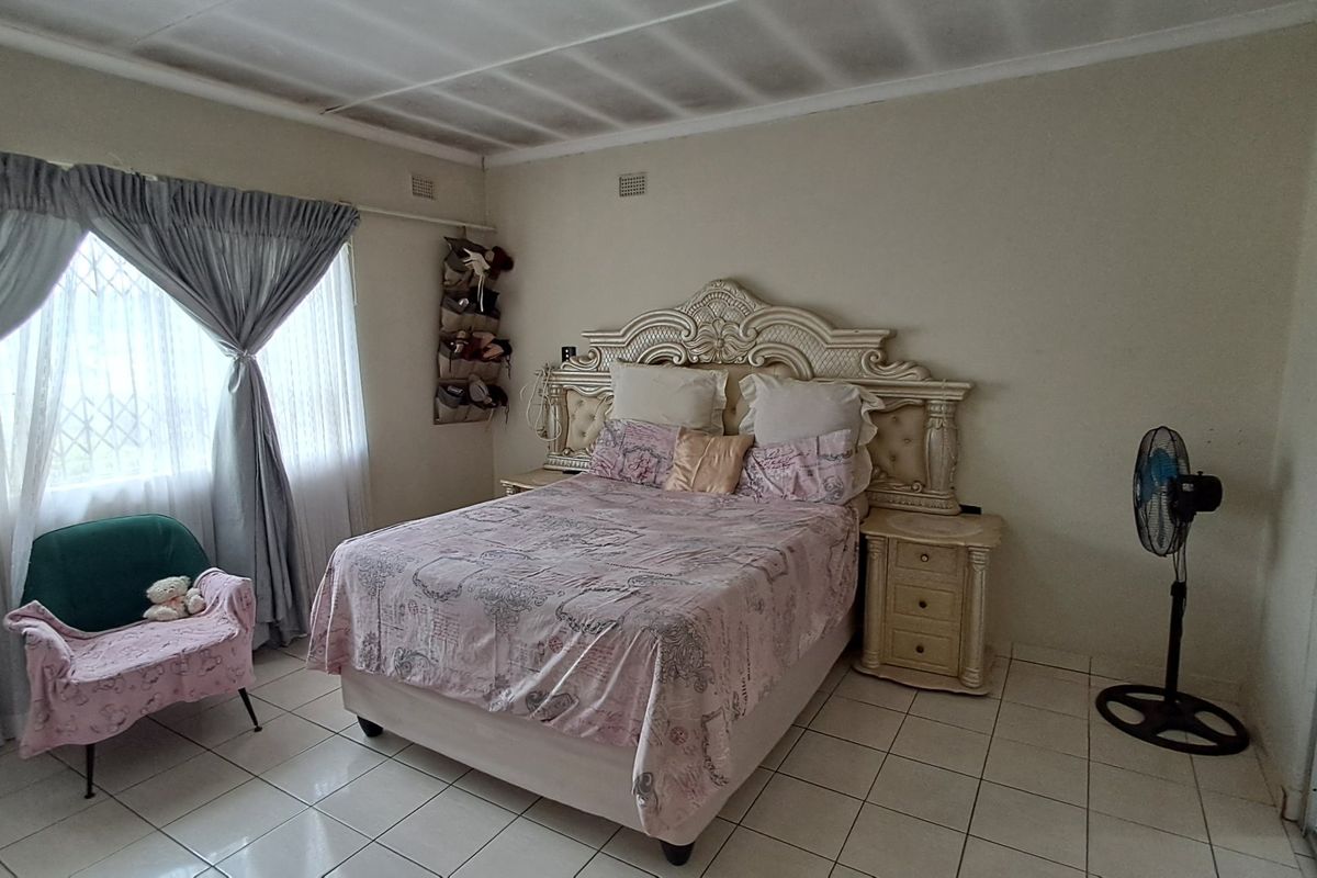 A bedroom featuring tiled flooring and a window with a security gate. The ceiling shows visible signs of water damage and cracking.