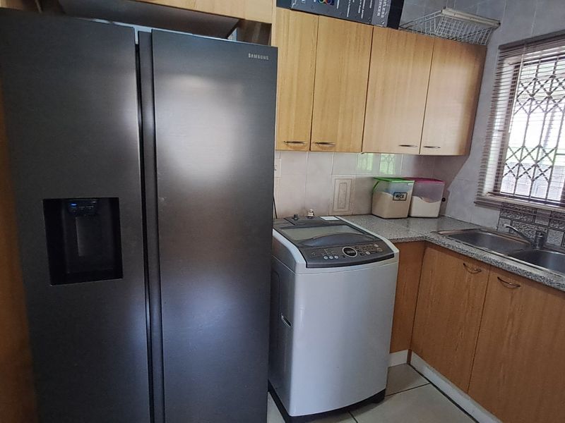 A functional laundry area featuring laminate cabinetry, granite countertops, a stainless steel sink, and a window with security bars.