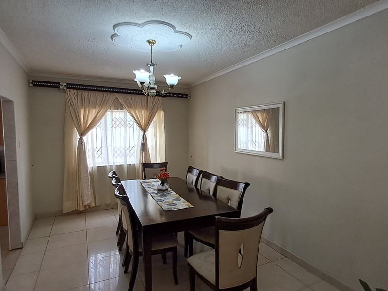 A dining room featuring ceramic floor tiles, a decorative ceiling rose with a chandelier, and a window fitted with a security gate.