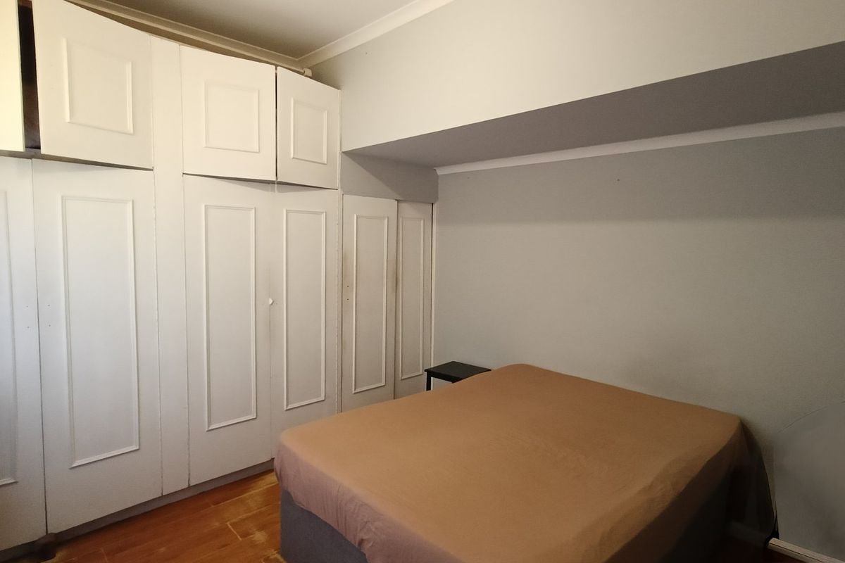 A bedroom featuring extensive white built-in cupboards and warm-toned wooden flooring, offering ample storage space.