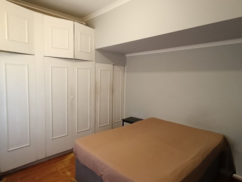 A bedroom featuring extensive white built-in cupboards and warm-toned wooden flooring, offering ample storage space.