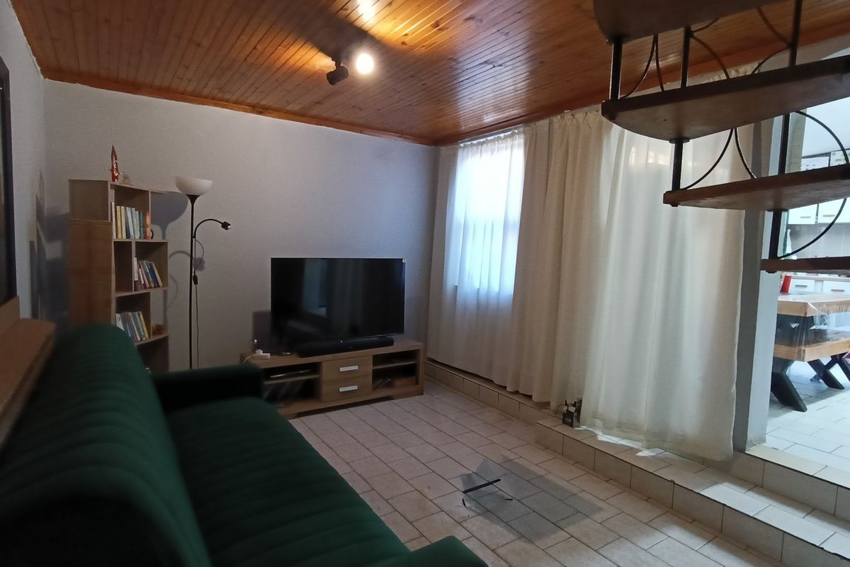 Living room featuring ceramic floor tiles and a timber ceiling, with an adjacent staircase leading to another level.