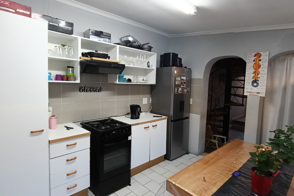 A functional kitchen featuring white cabinetry, tiled backsplash, a gas stove with extractor fan, and tiled flooring, leading to an arched entryway.
