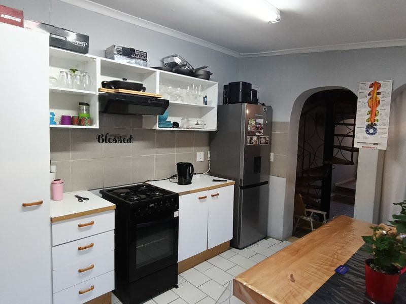 A functional kitchen featuring white cabinetry, tiled backsplash, a gas stove with extractor fan, and tiled flooring, leading to an arched entryway.