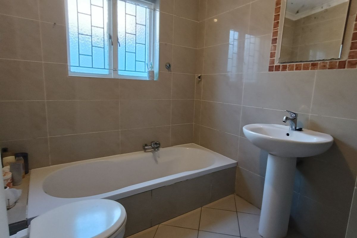 A functional bathroom featuring a bathtub, pedestal basin, and neutral wall tiling with a window providing natural light.