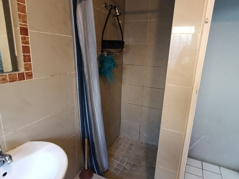 A functional bathroom featuring a tiled shower enclosure, pedestal basin with mixer tap, and wall-mounted mirror.