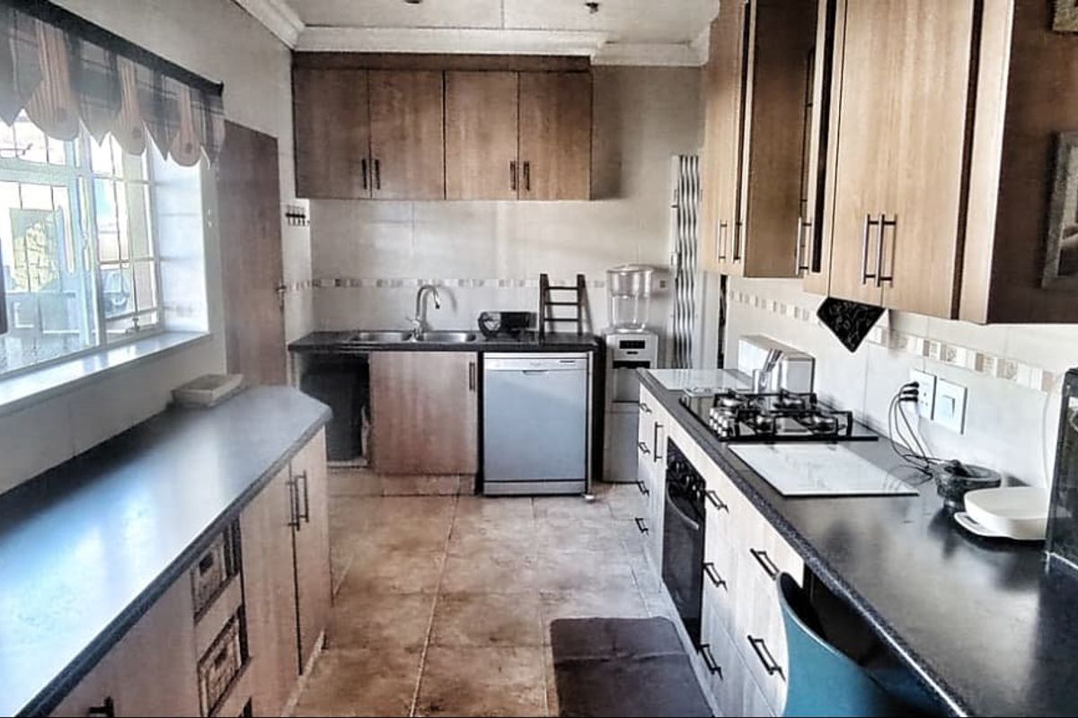 A functional kitchen featuring wooden cabinetry, dark countertops, a gas hob, built-in oven, and tiled flooring with a practical layout.