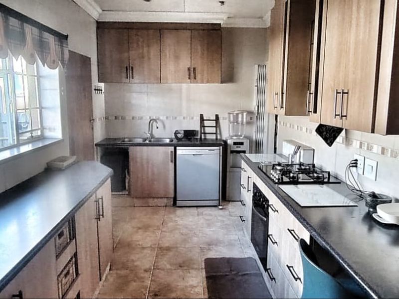 A functional kitchen featuring wooden cabinetry, dark countertops, a gas hob, built-in oven, and tiled flooring with a practical layout.