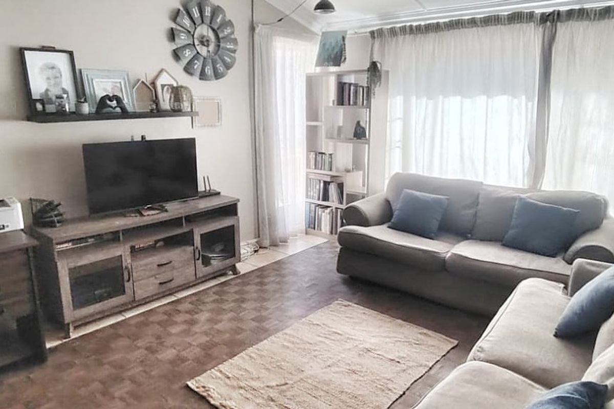 A comfortable living room featuring tiled flooring and large windows, providing a functional space for relaxation and home office activities.