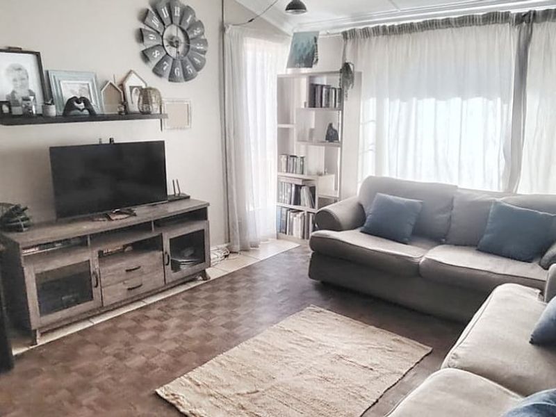 A comfortable living room featuring tiled flooring and large windows, providing a functional space for relaxation and home office activities.