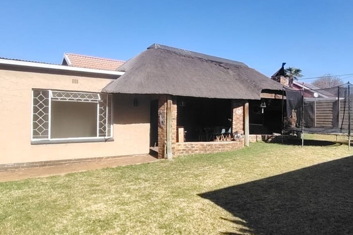 Rear view of the property featuring a covered patio with a thatched roof, a private garden, and secure boundary walling.