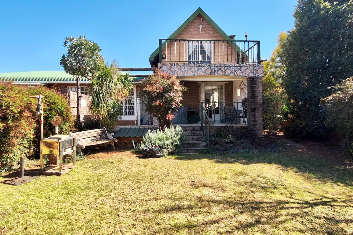 Rear view of the house featuring a brick facade, an upper-level balcony with metal railings, and a spacious garden area.