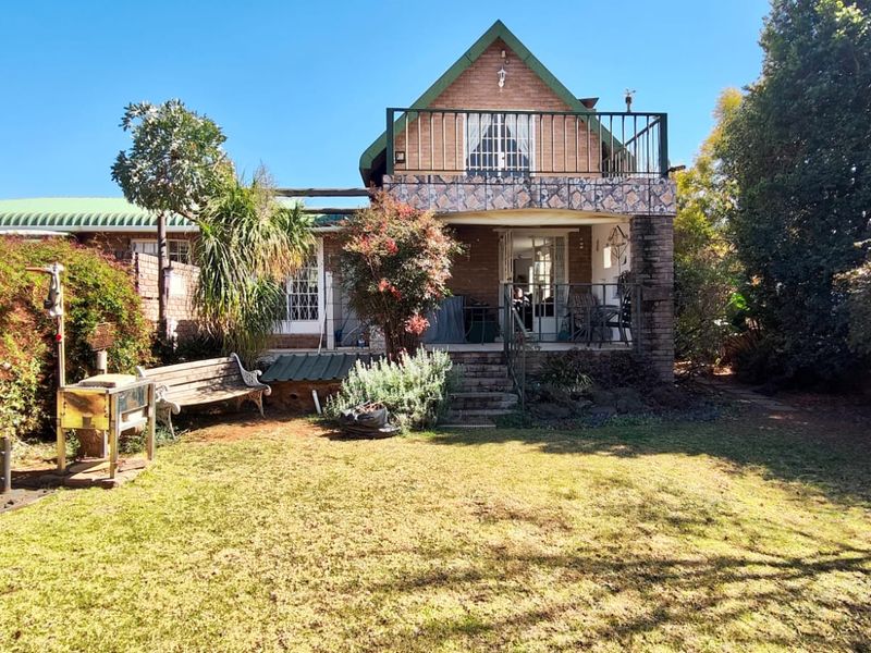 Rear view of the house featuring a brick facade, an upper-level balcony with metal railings, and a spacious garden area.