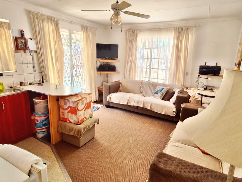 Open-plan living area featuring a compact kitchen corner with cabinetry and sink, integrated with a comfortable lounge space and ceiling fan.