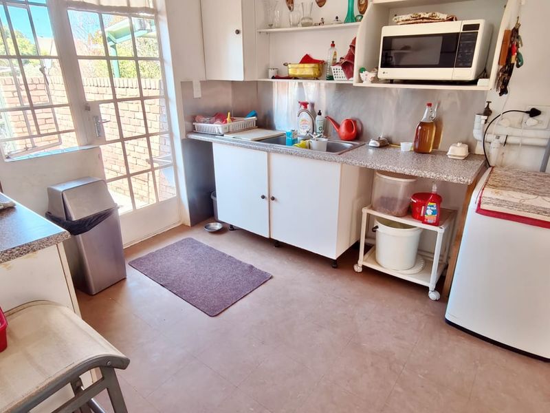 A functional scullery area featuring laminate countertops, a stainless steel sink, and direct access to the exterior through a glass-paneled door.