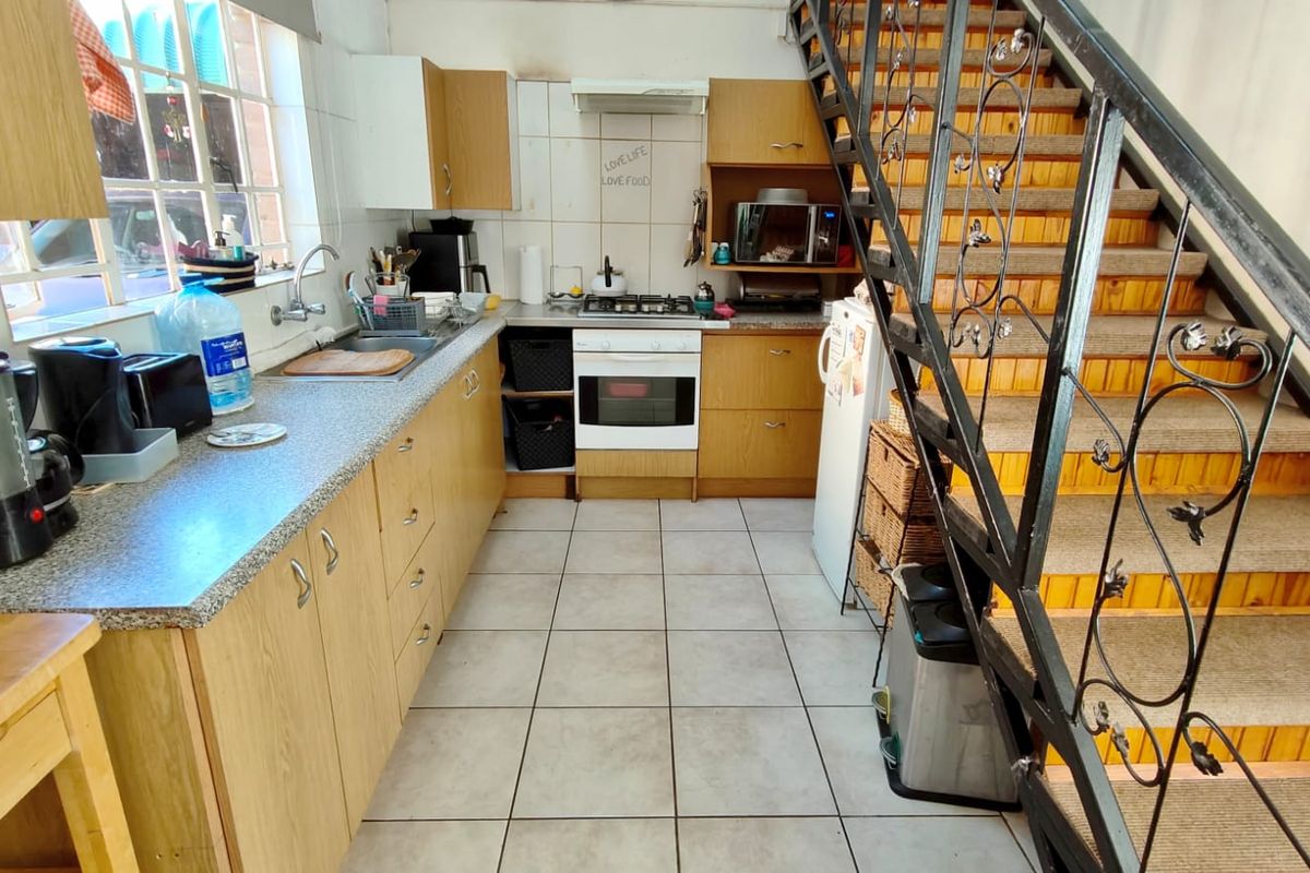 Functional kitchen featuring laminate cabinetry, built-in oven and hob, tiled flooring, and an adjacent staircase with wrought iron railing.