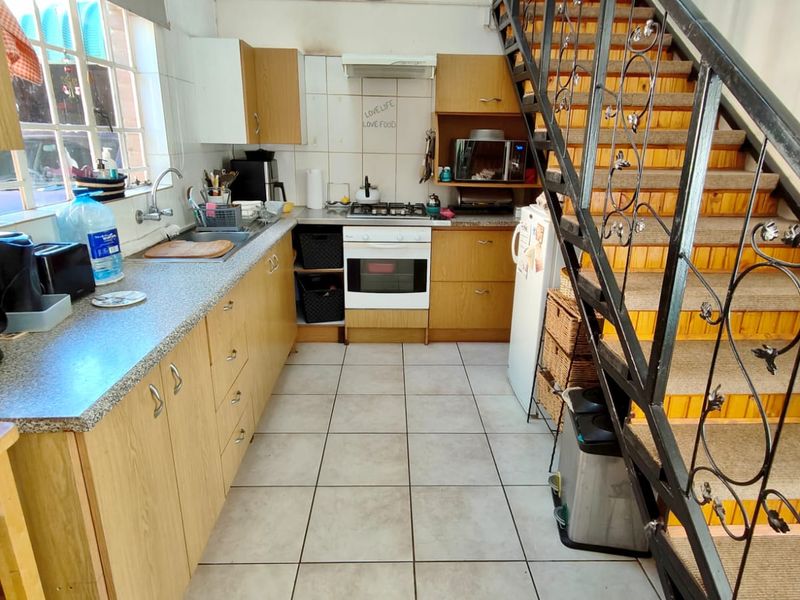 Functional kitchen featuring laminate cabinetry, built-in oven and hob, tiled flooring, and an adjacent staircase with wrought iron railing.