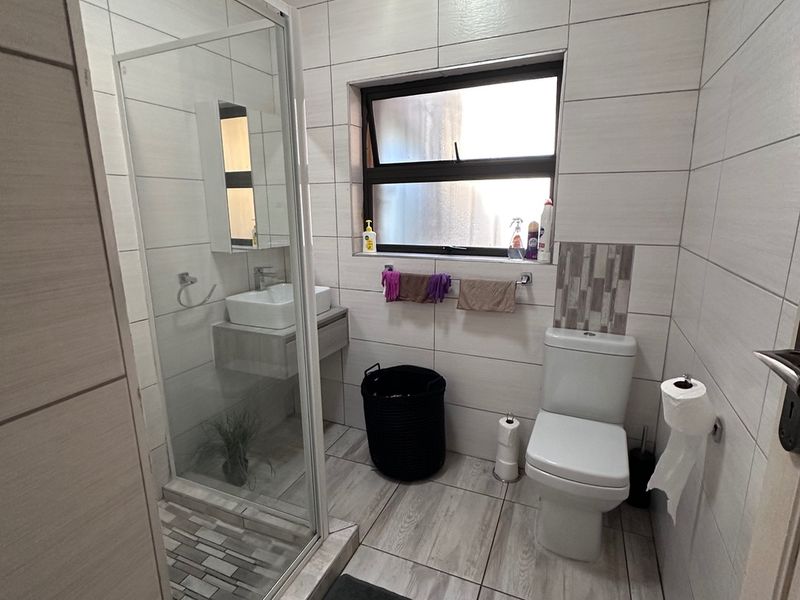 A compact bathroom featuring a glass shower enclosure, modern vanity basin, and toilet, with neutral tiled finishes and an unfinished ceiling perimeter.