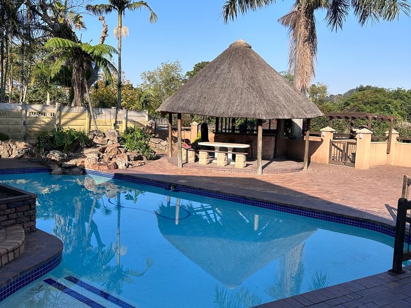 Outdoor pool area featuring a swimming pool, brick paved surround, and a traditional thatched lapa structure for entertainment.